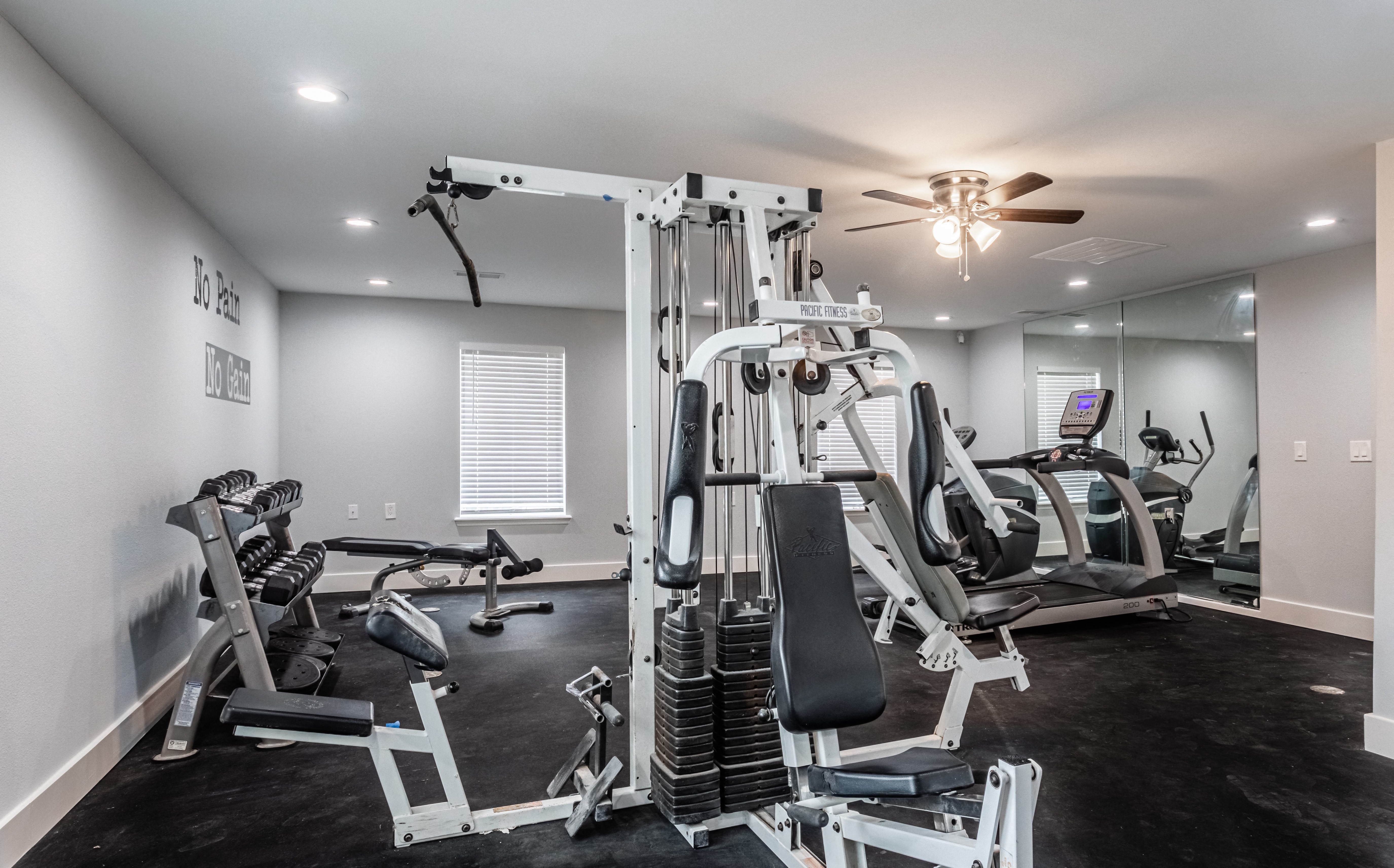 a gym with cardio machines and a ceiling fan